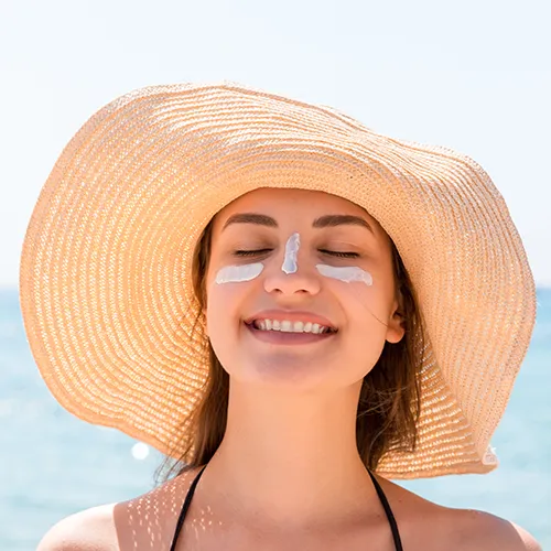 Woman walking on the beach with a wide-brimmed hat for sun protection.