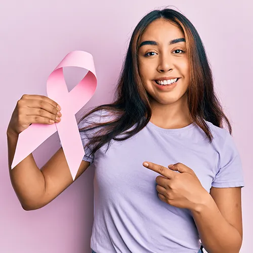 Mujer latina joven sosteniendo un lazo rosa contra el cáncer sonriendo feliz señalando con la mano y el dedo